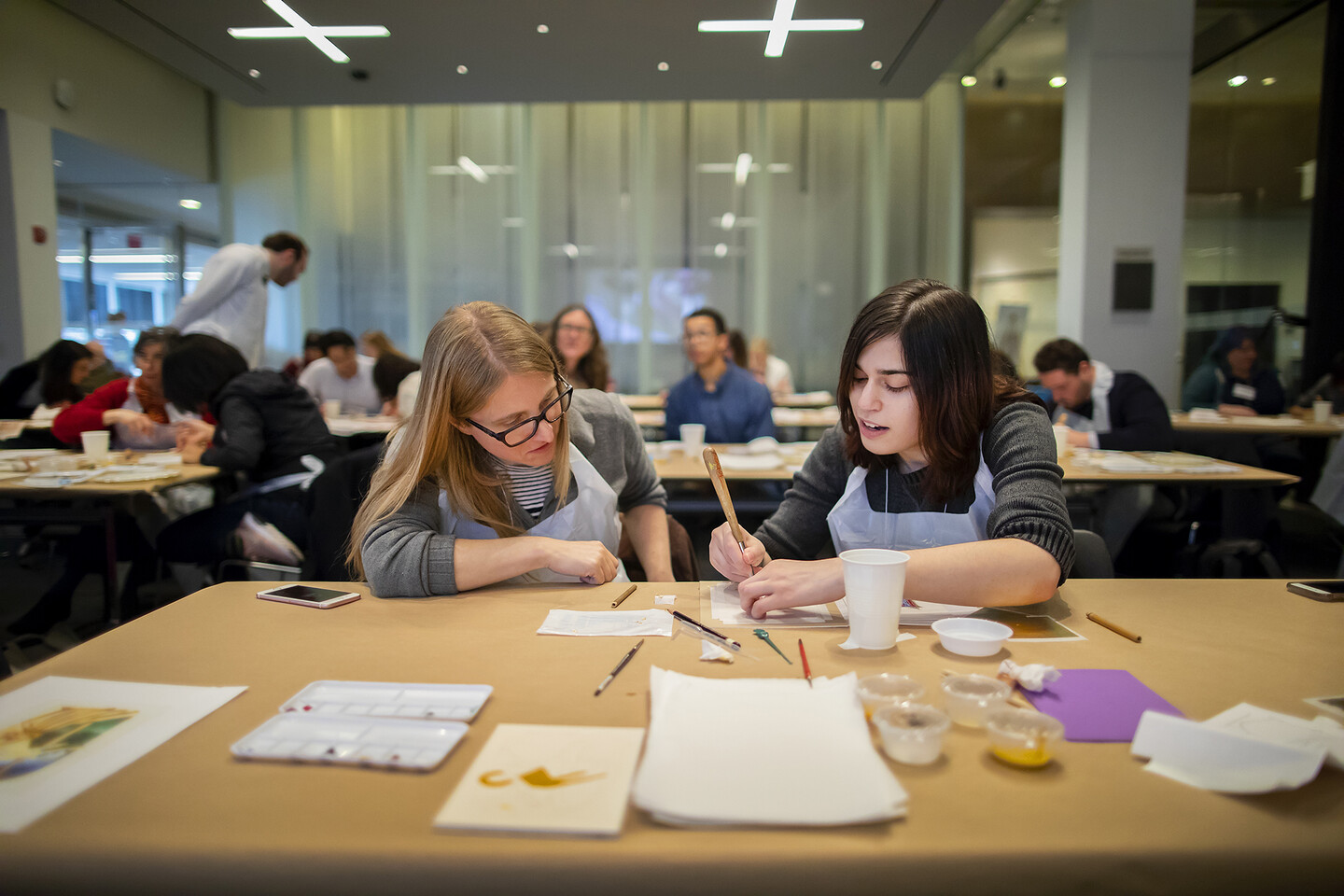 two women sitting at a table working with materials to make illuminated manuscript letters
