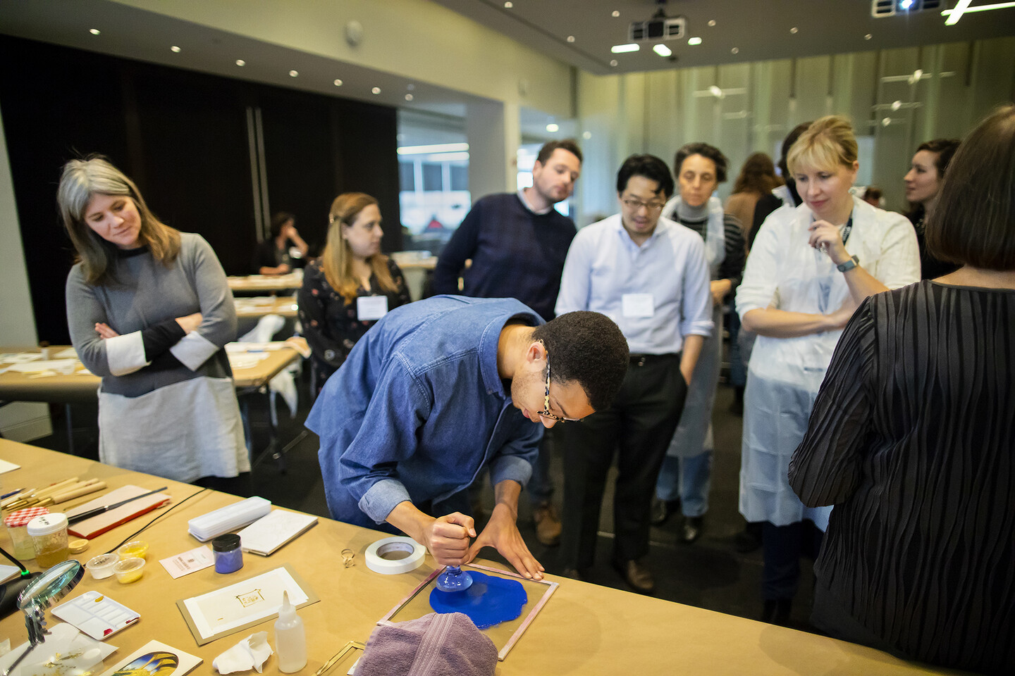 onlookers watch student working with blue ink and tools on a table