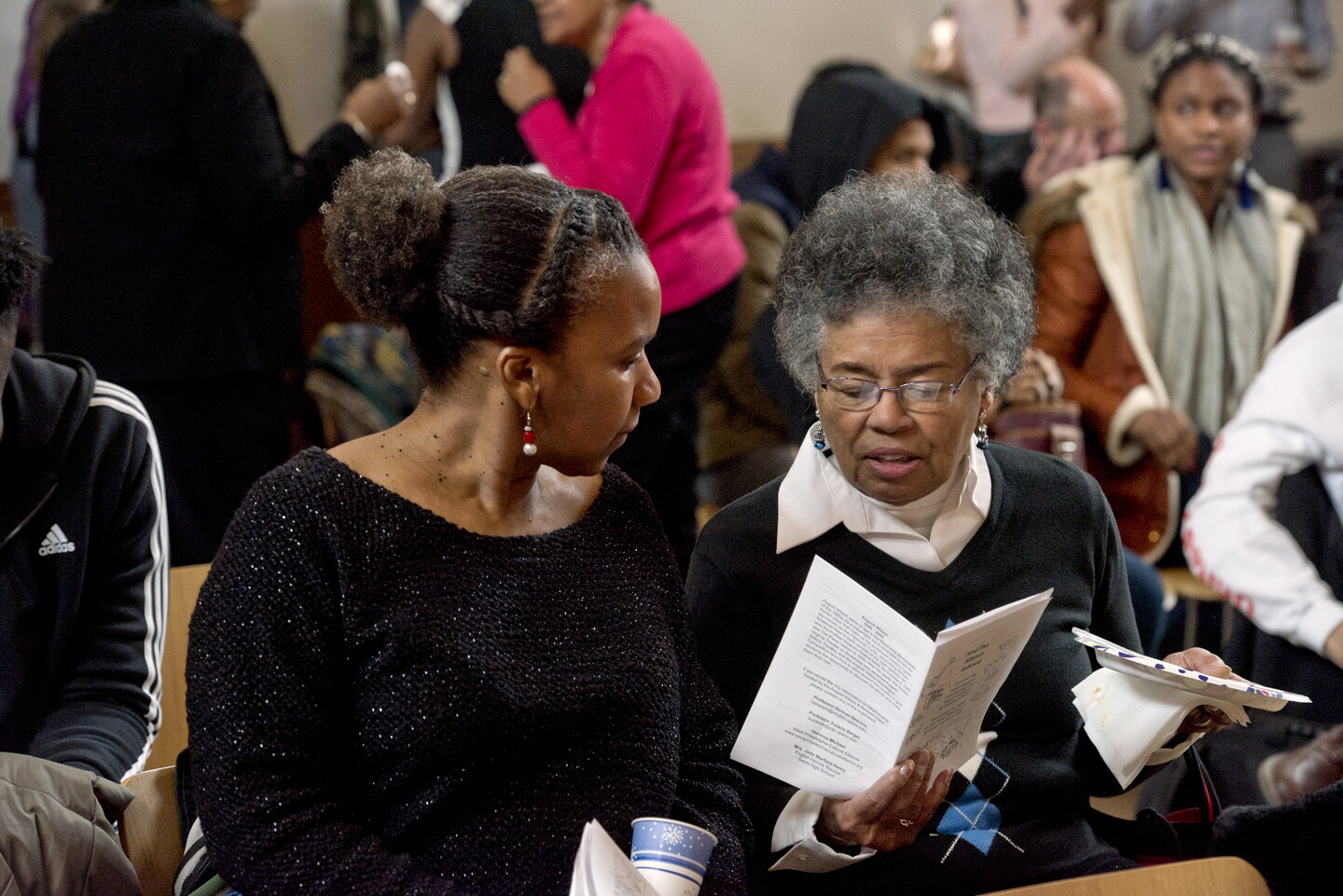 two women seated in the audience of the auditorium with one holding a playbill and reading from it