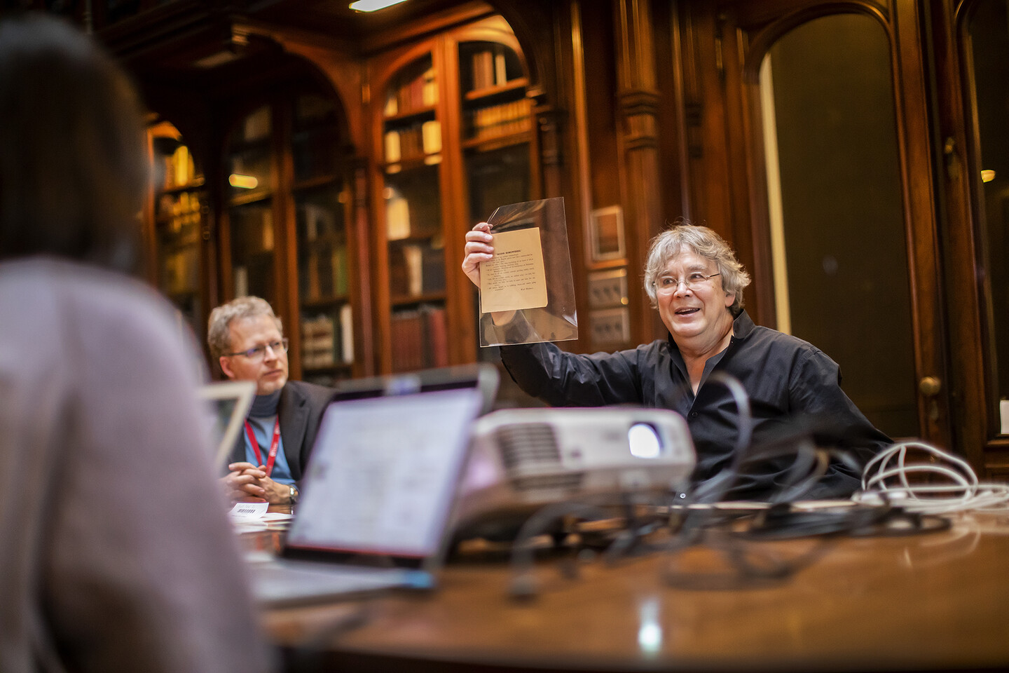 Professor holding up printed rare document for students to view. 