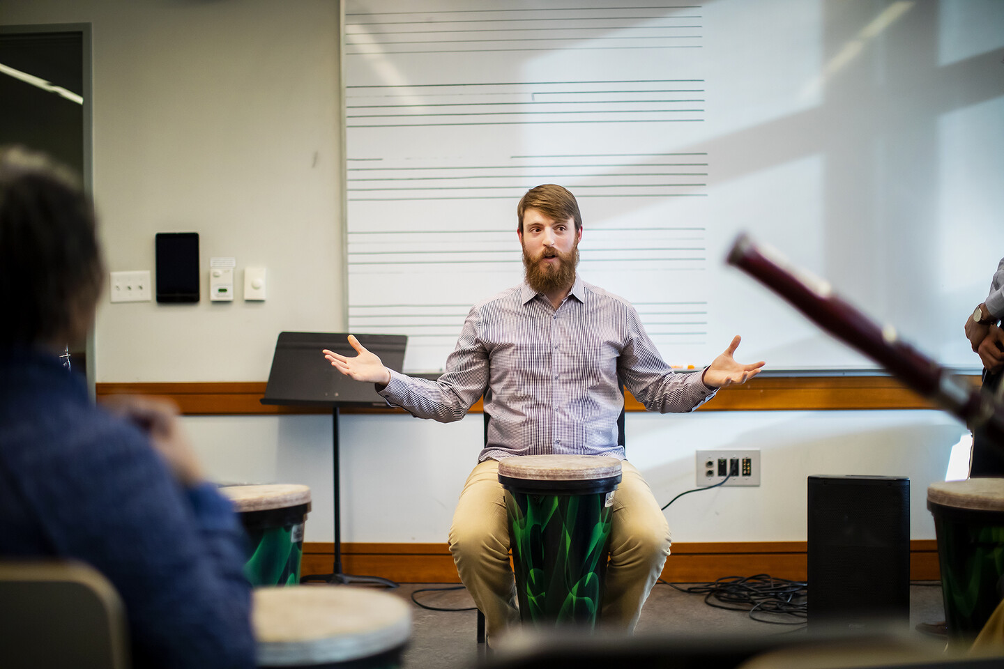 A man with him arms wide open, in front of a drum, with a bassoon in the foreground.