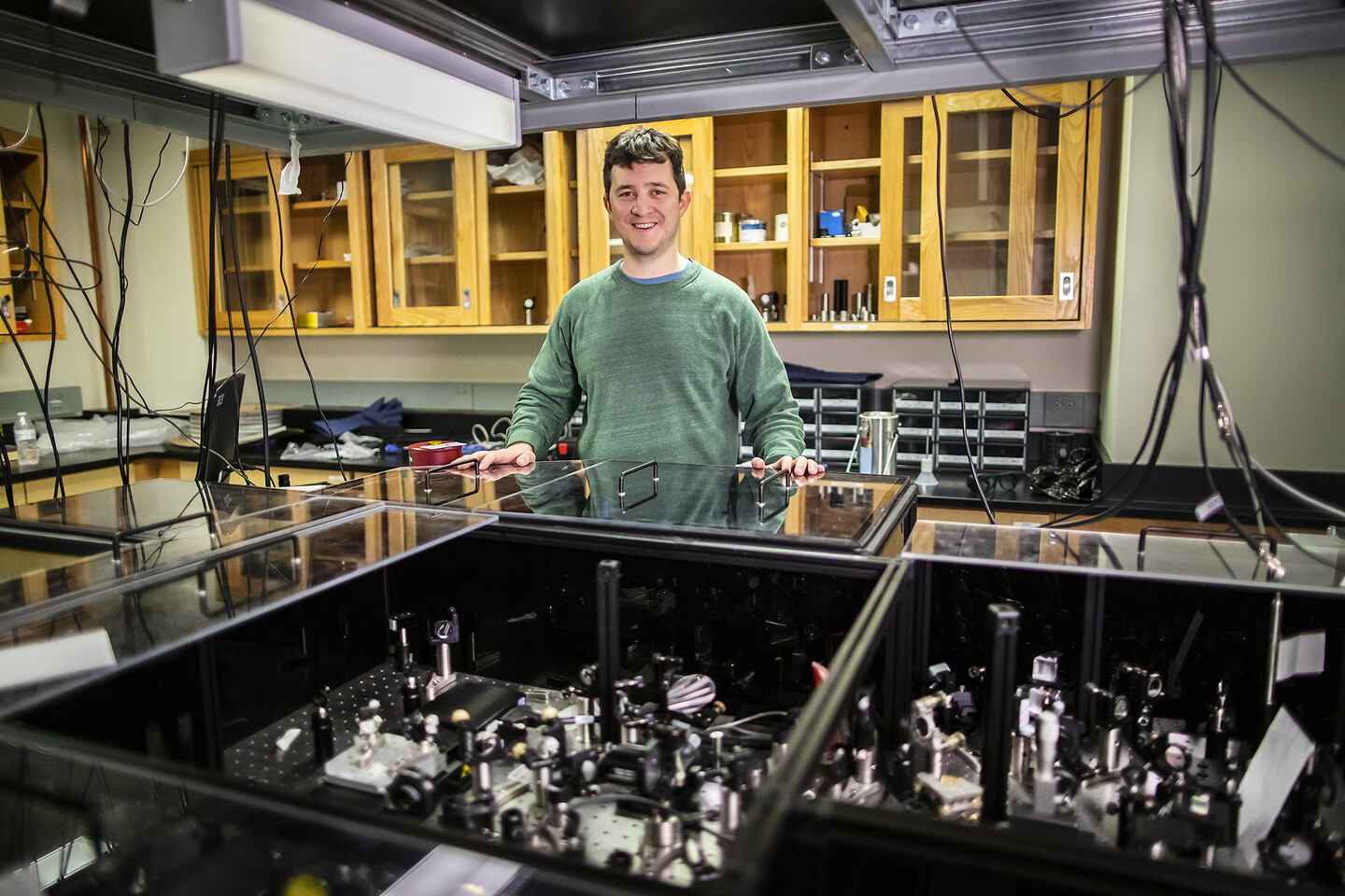 meloni in a lab standing behind a table covered with mirrors and lenses
