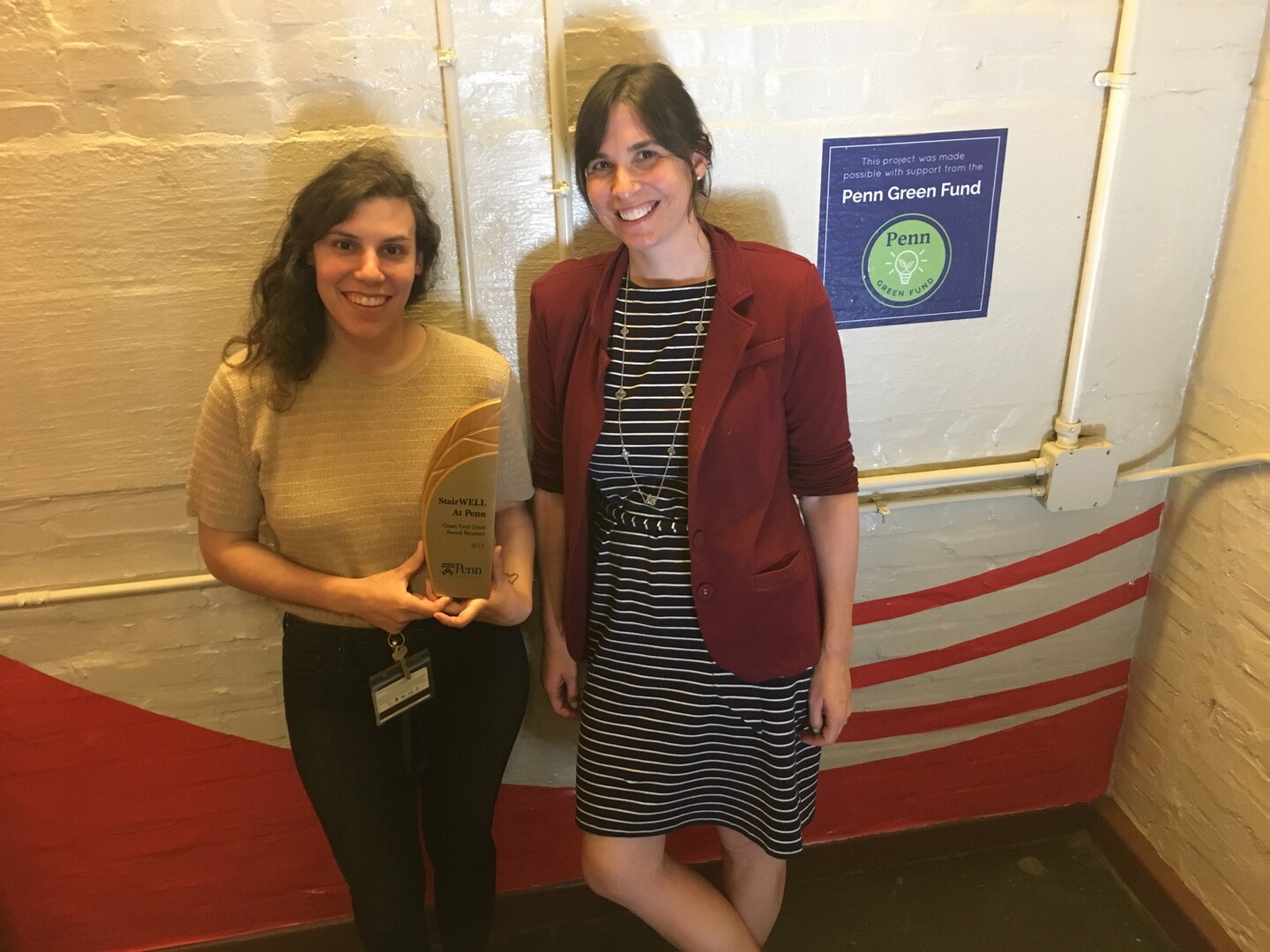 Sara and Danielle in a stairwell beside a Green Fund poster