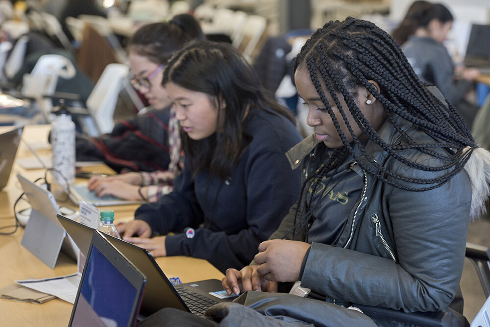 Students at Femmehacks work intensely on their laptops