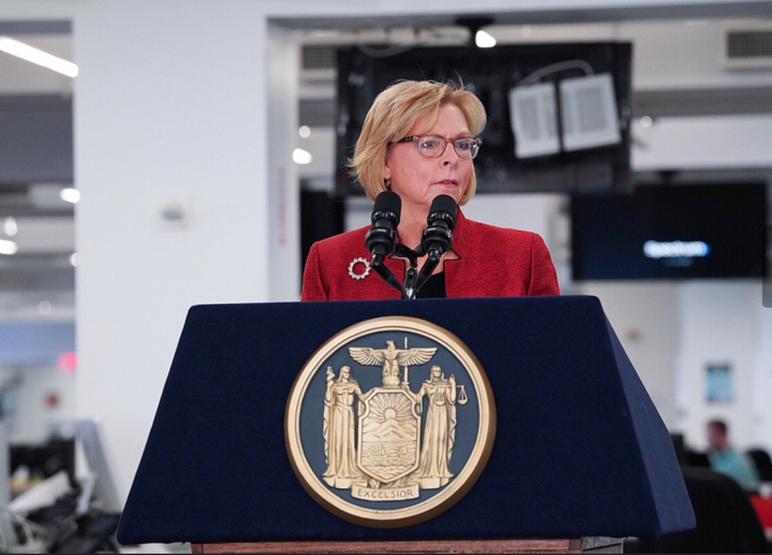 Woman in a red jacket standing at a podium with two microphones. 
