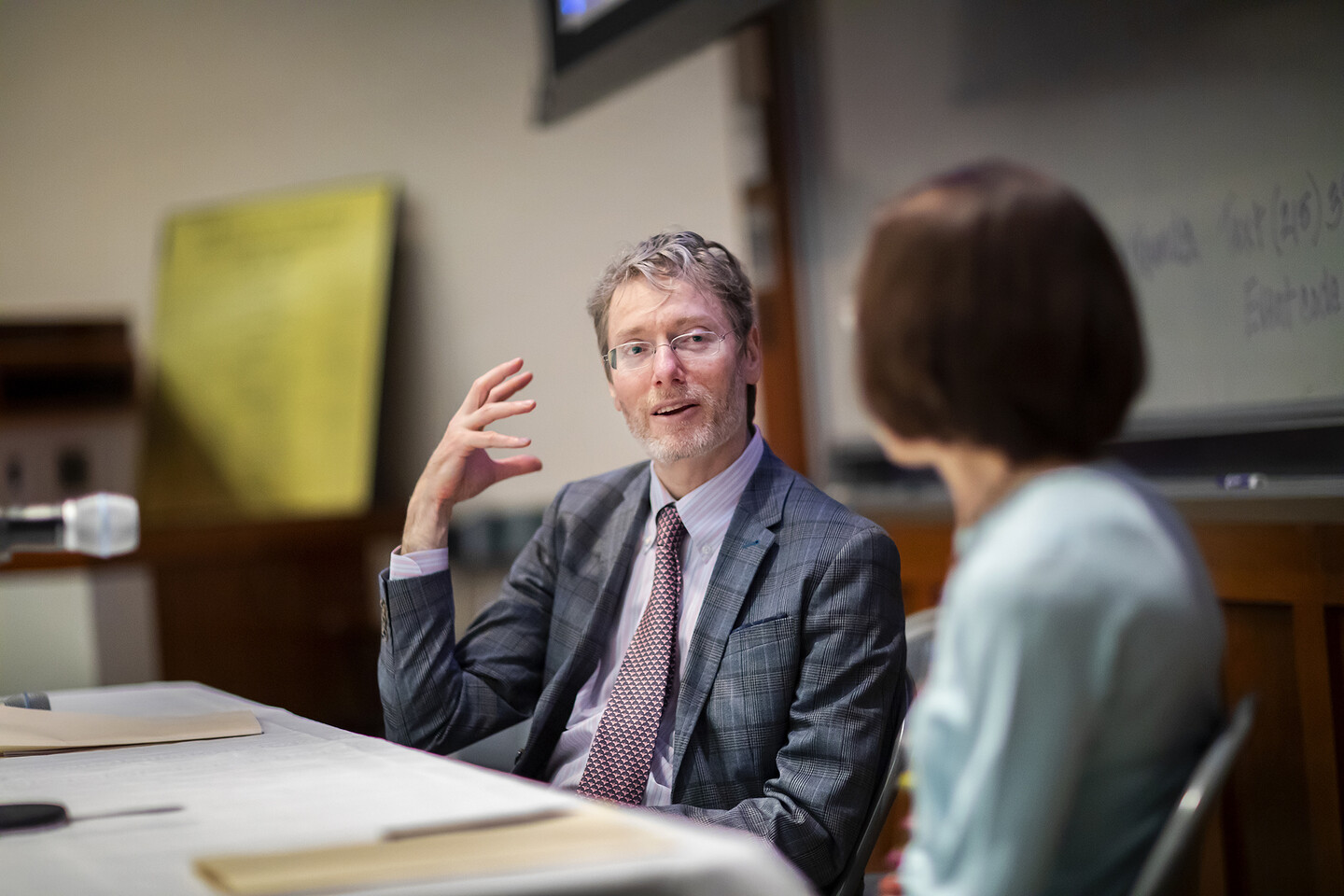 A man gesturing with his hand while talking to a woman whose back is to us. 