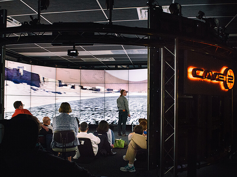 Audience members watch a panoramic film on a very wide, paneled screen