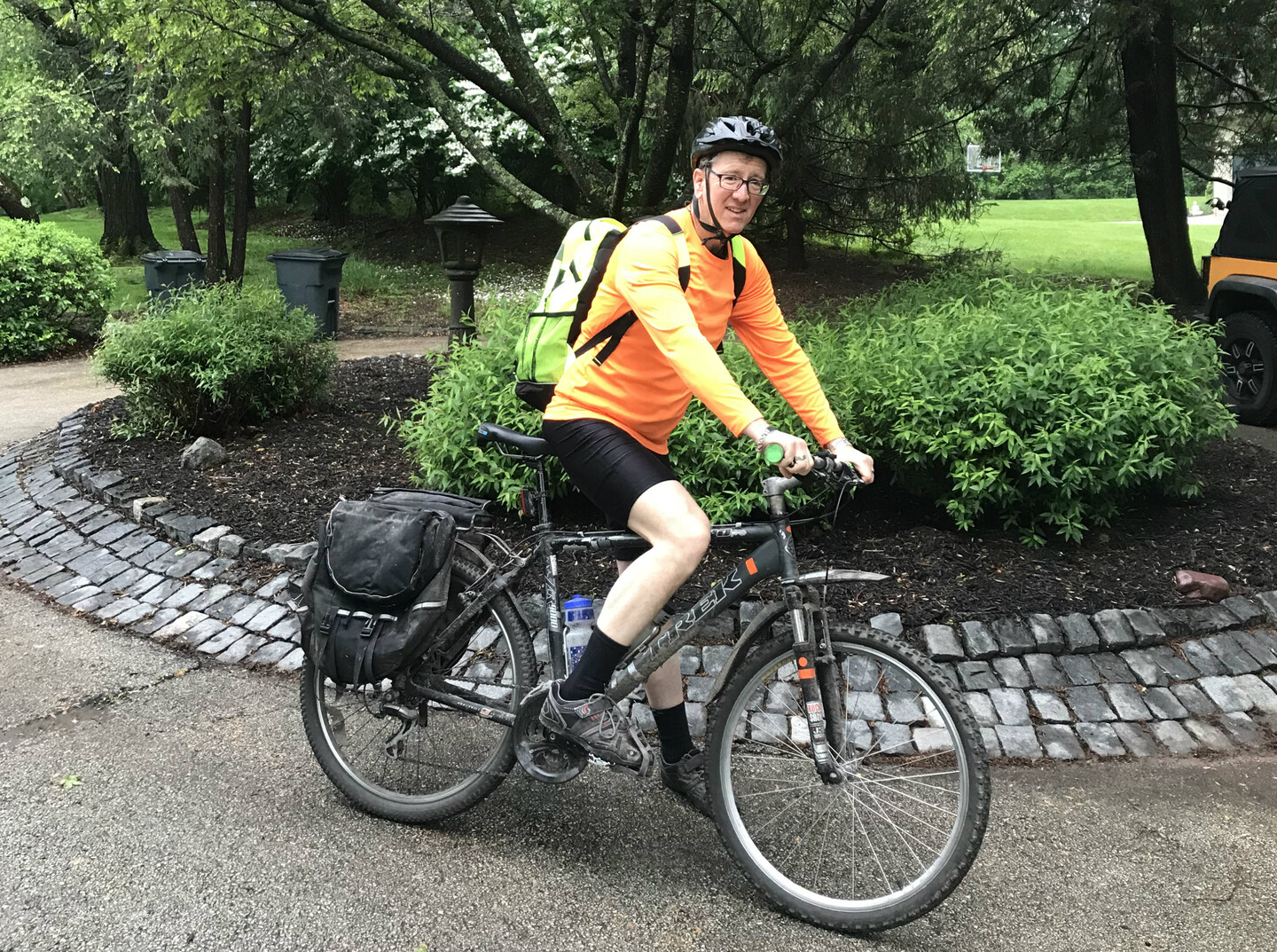 A person on a bike loaded with cargo bags and a water bottle looks at the camera