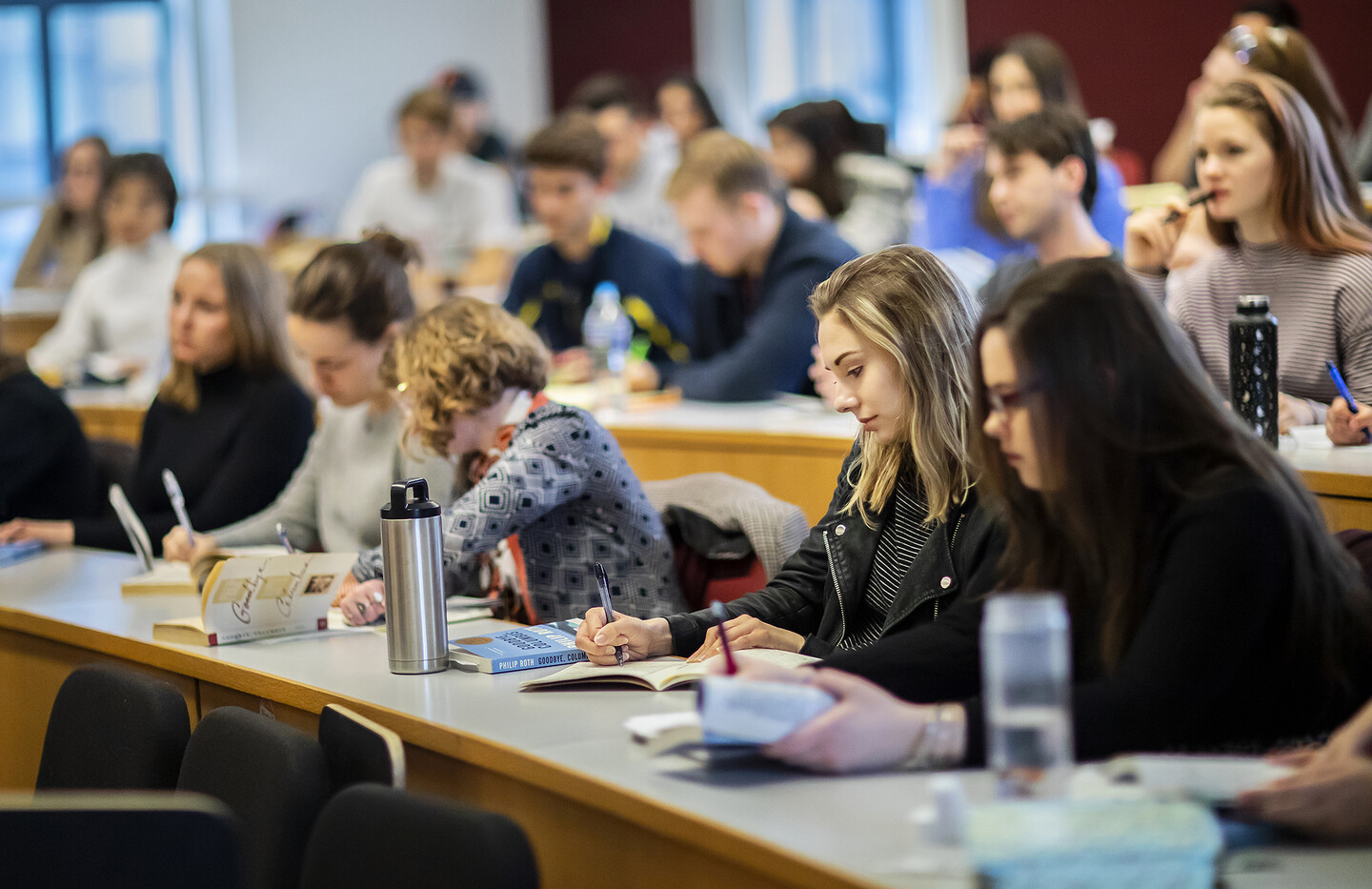 Rows of students in class, writing in notebooks. 