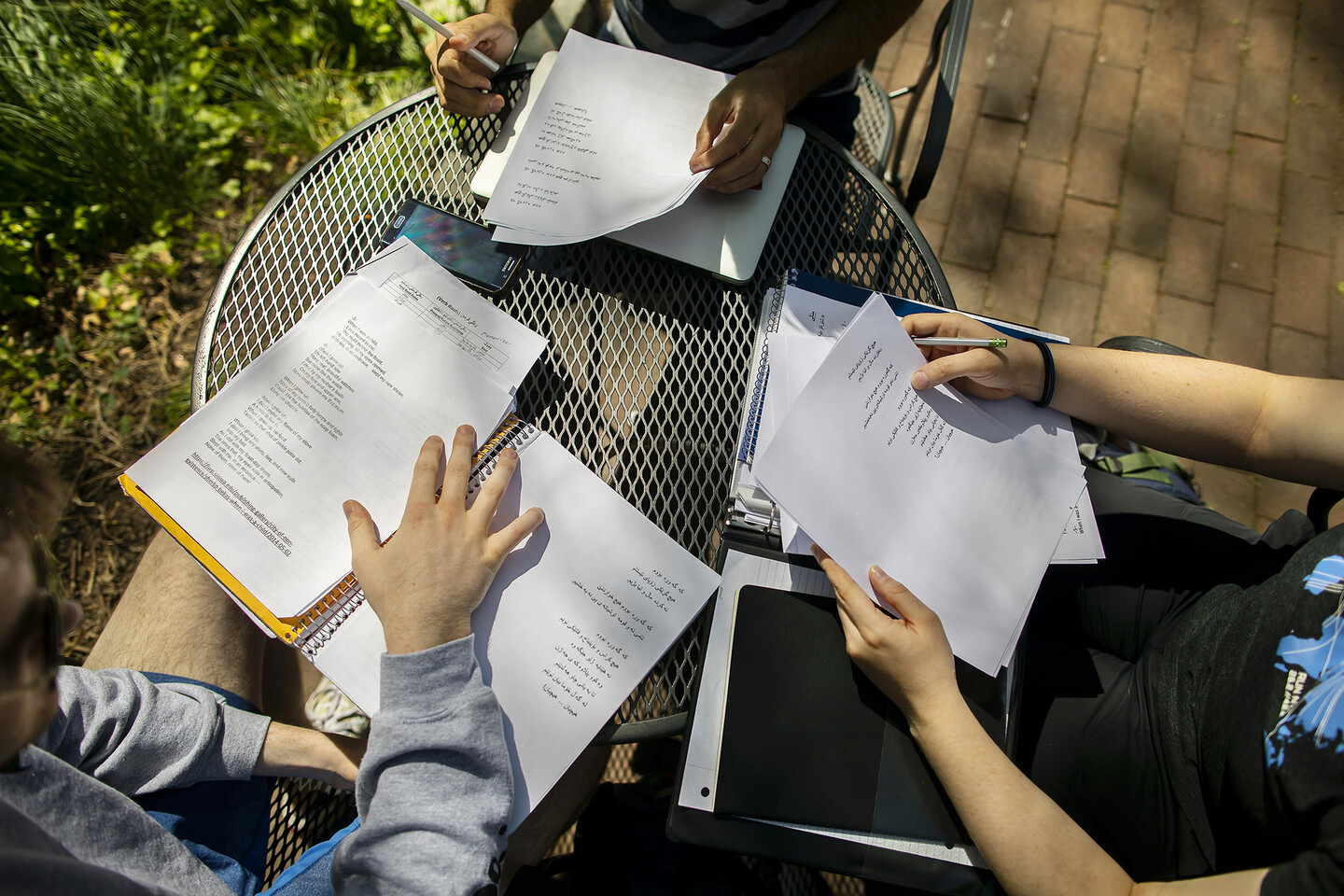 Papers on a table with Arabic script and the hands of there people around a small table. 