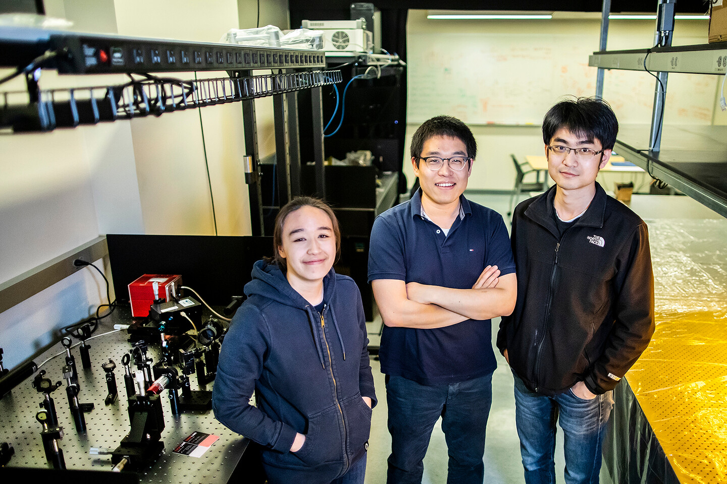 yoshioka, zhen, and he standing next to an optics table