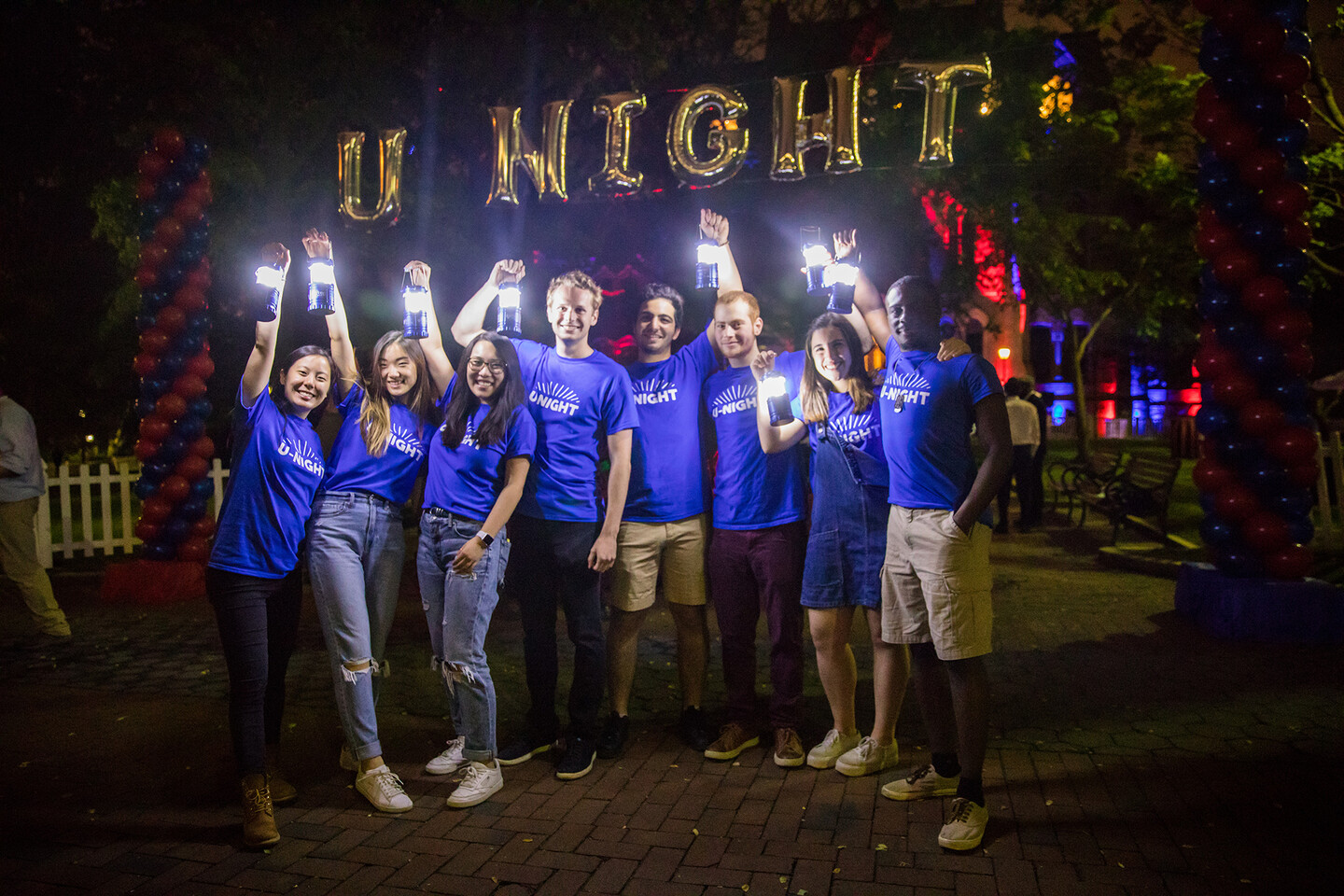 Students holding up small lanterns at night underneath balloons reading U NIGHT
