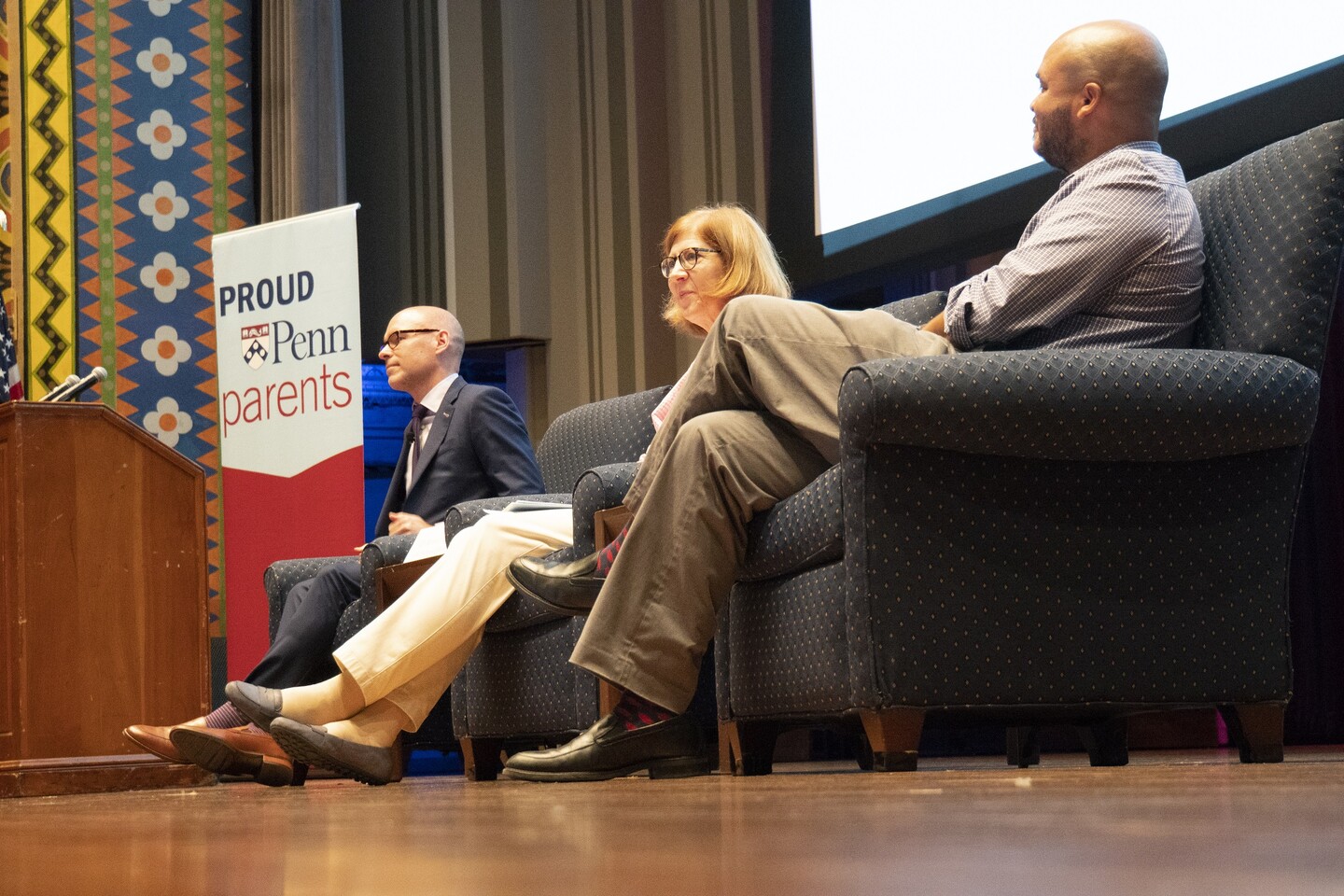 Penn administrators on stage chatting with sign that reads 'Proud Penn Parents'