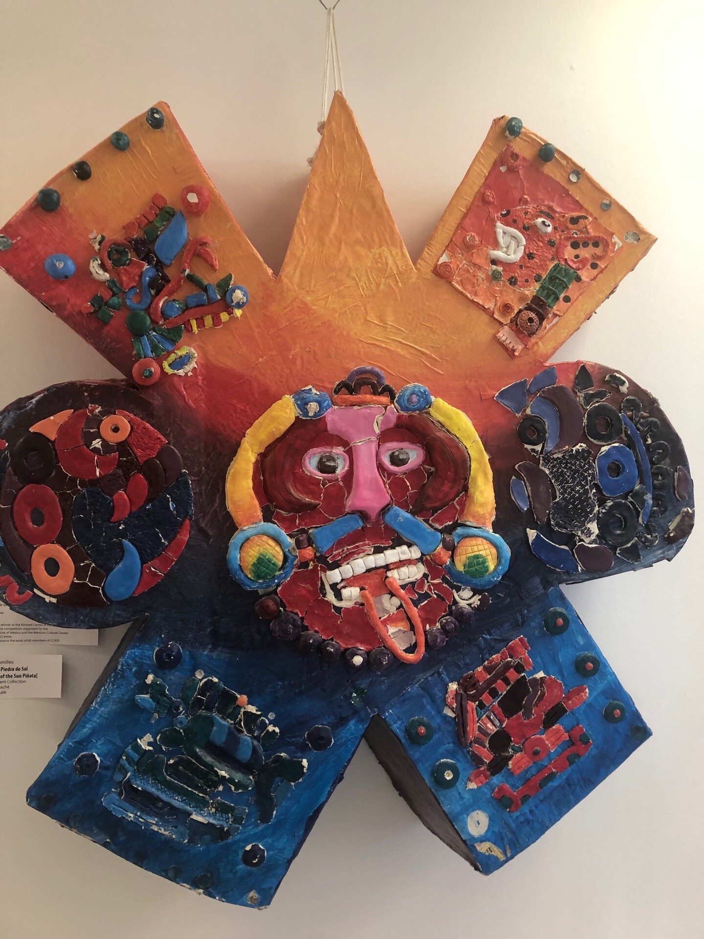 Art piece hangs on wall, portraying a person's head surrounded by a cluster of shapes and symbols