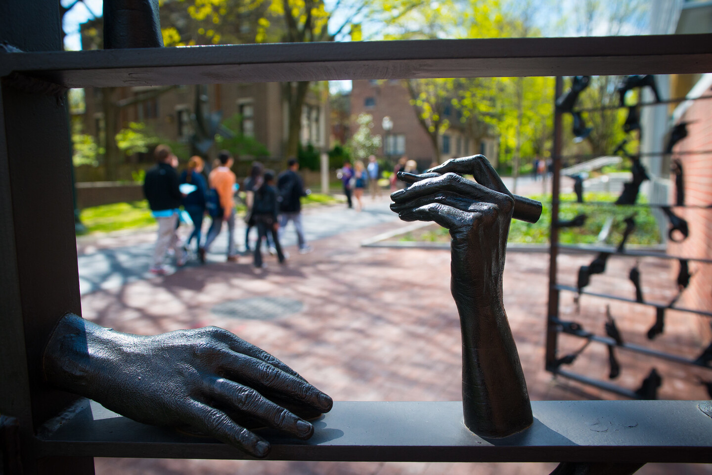 A closeup of a detail on a metal gate showing two hands, one holding a pencil.. 