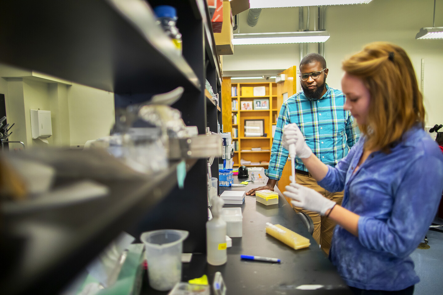A scientist observes another pipetting material at a lab bench
