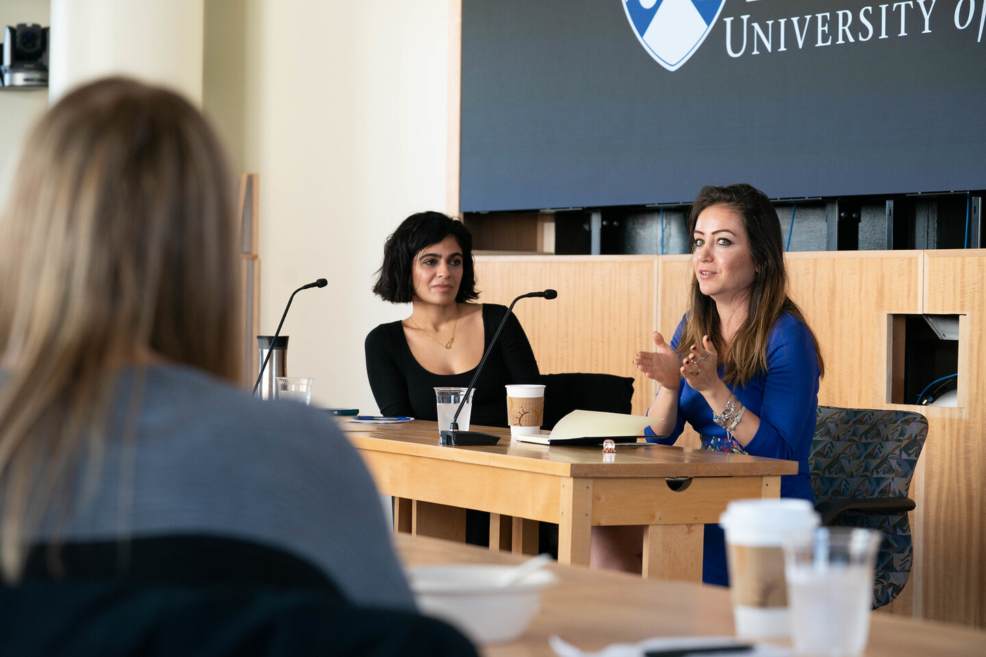 Two people speaking at a desk to a member of an audience. 