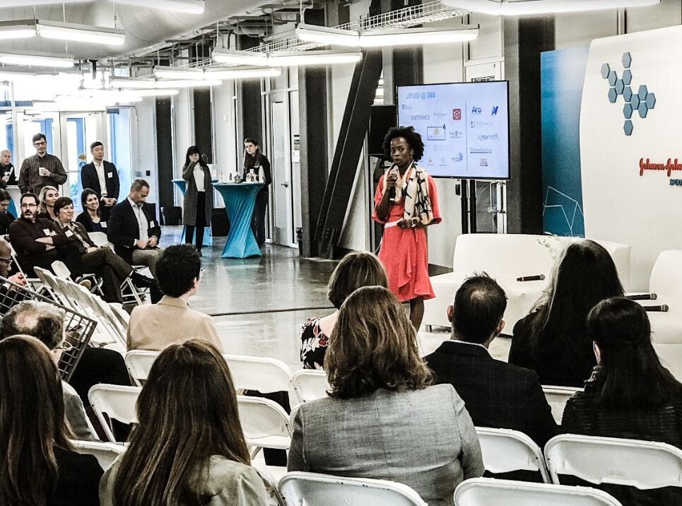 a person speaks into a microphone in front of an audience in an open office setting