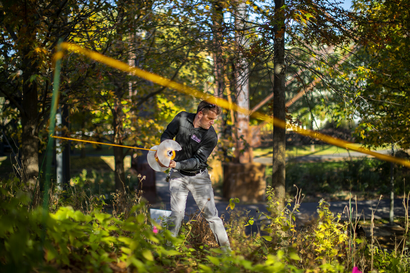 A person arranges ropes off a study area outdoors, surrounded by trees.