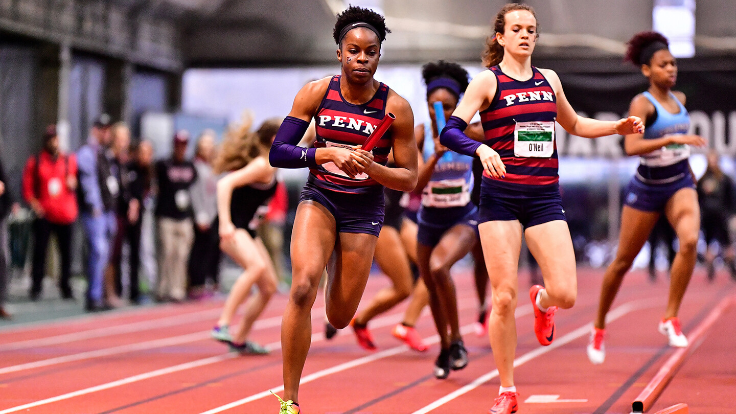 Cecil Ene of the track and field team runs around an indoor track after receiving the relay baton.