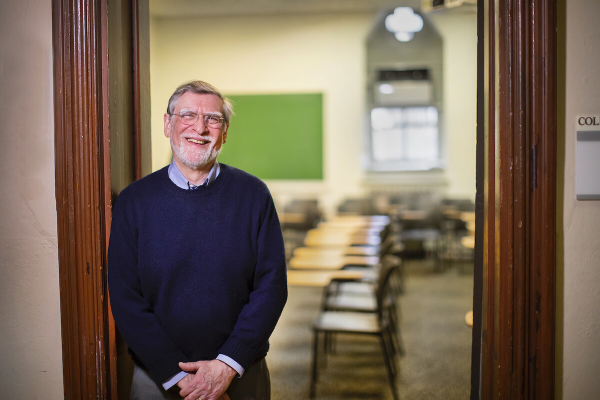 Person leans in doorway, behind them is a classroom full of empty desks