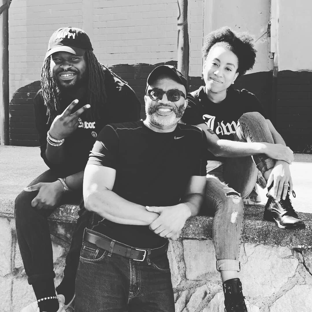 Three people sitting outside on a concrete ledge in front of a painted wall.