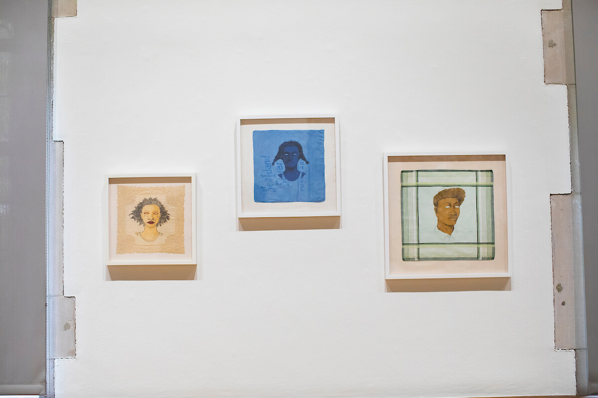 Three paintings, each with a portrait of one person, hanging on a wall