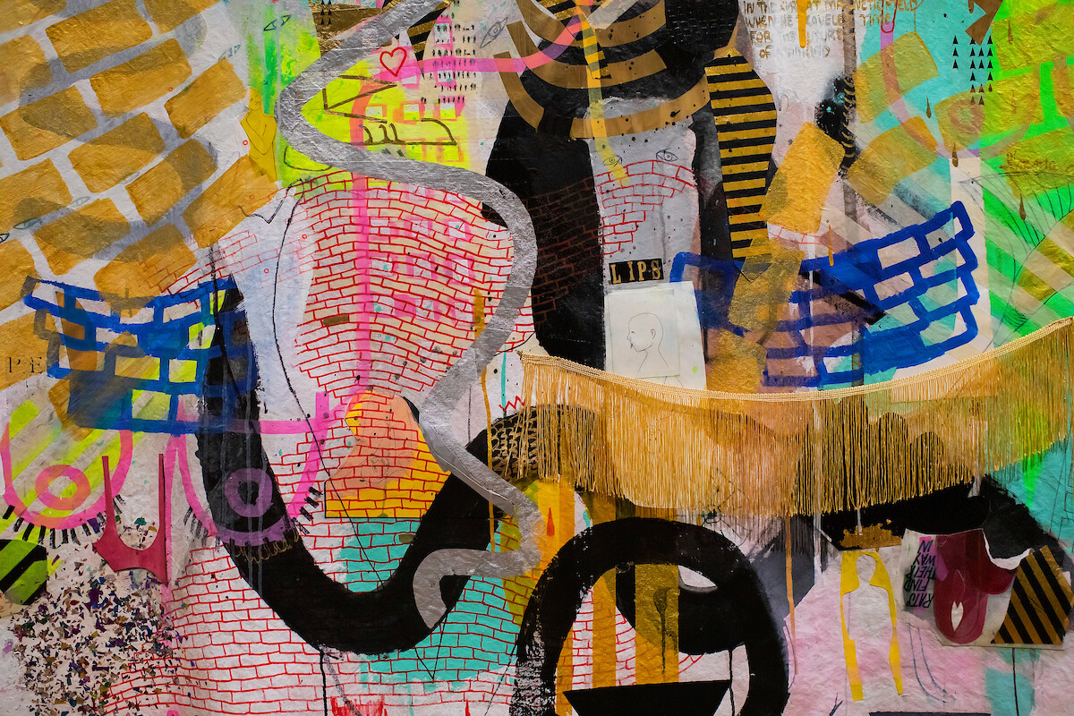 Close up of artwork with many shapes and colors and a strand of gold fringe