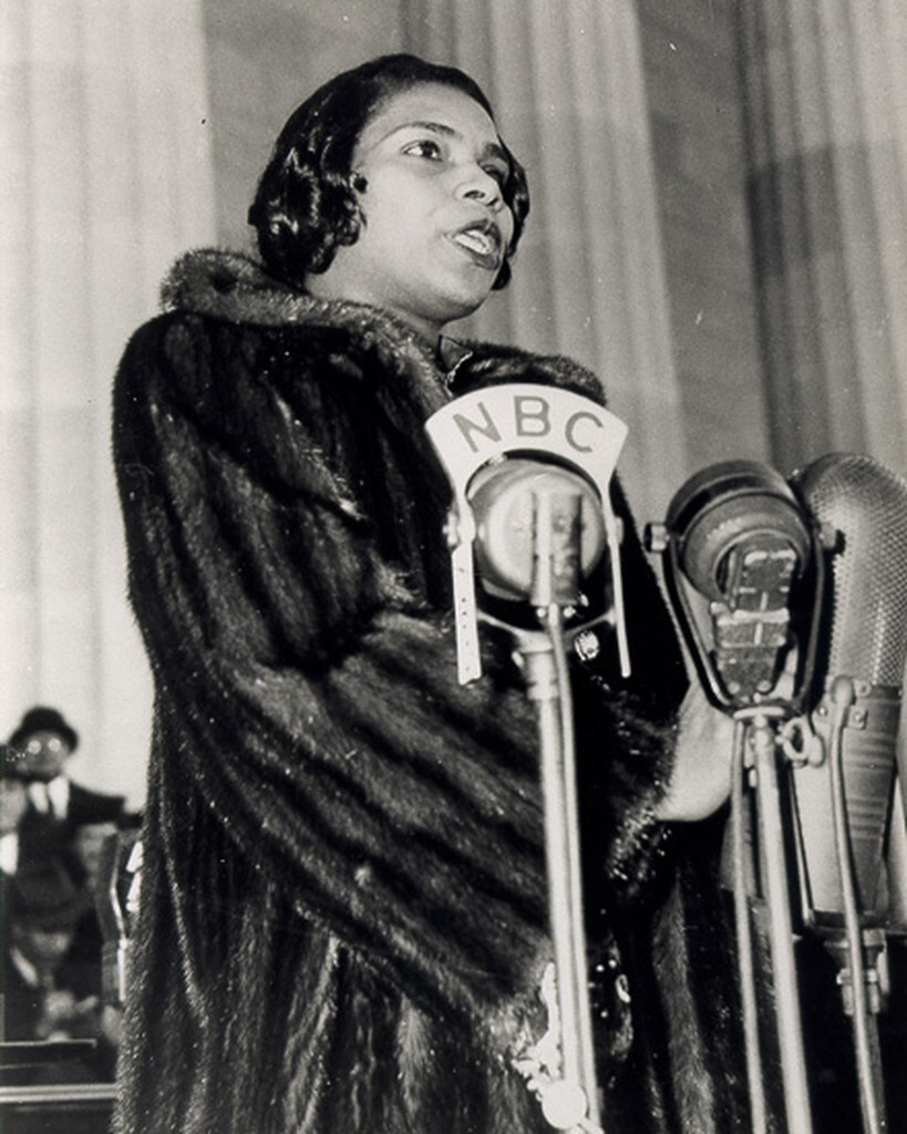 Woman in a fur coat sings before several microphones; one says 'NBC'