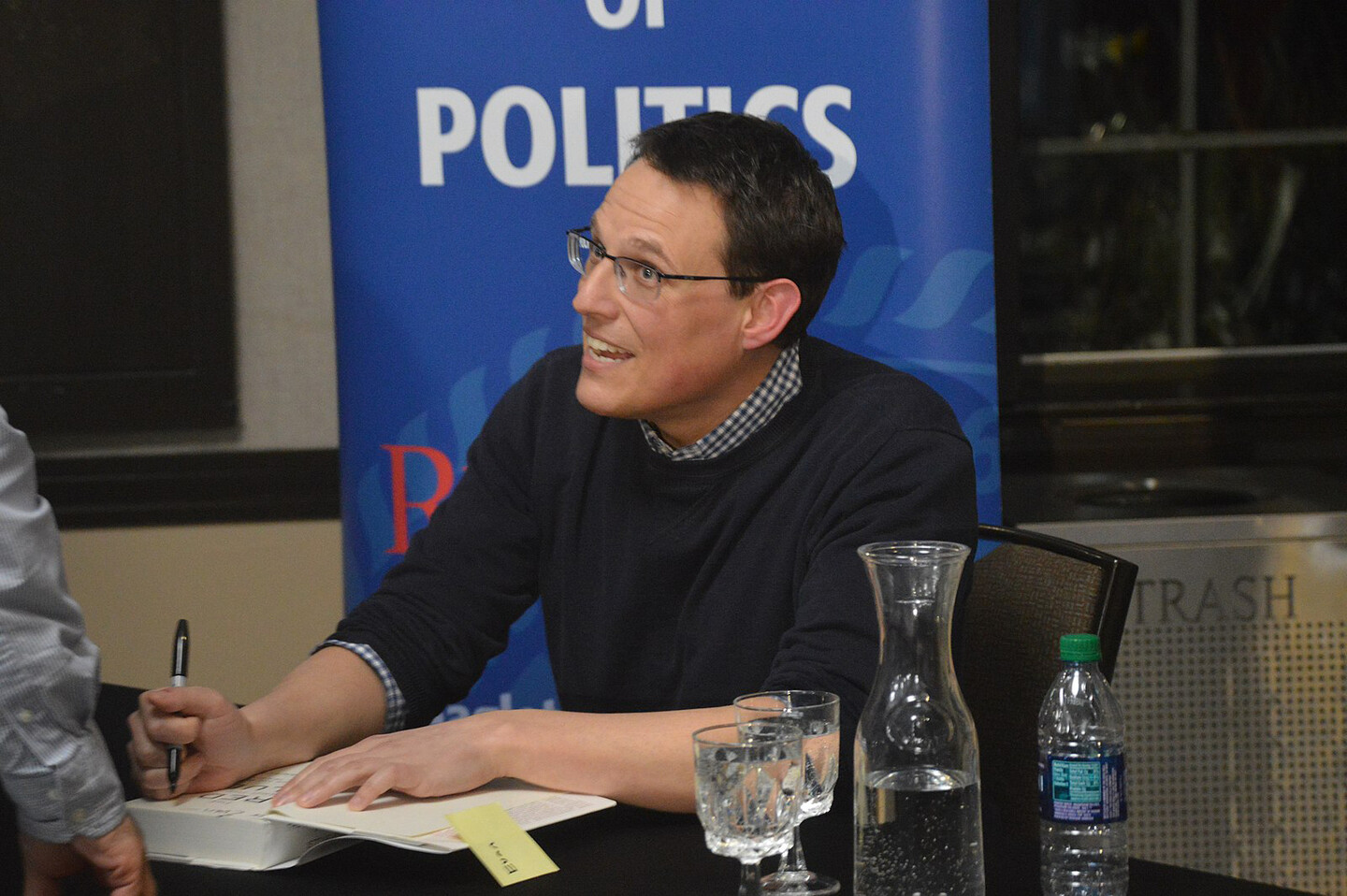Steve Kornacki talks while signing a book on a table.