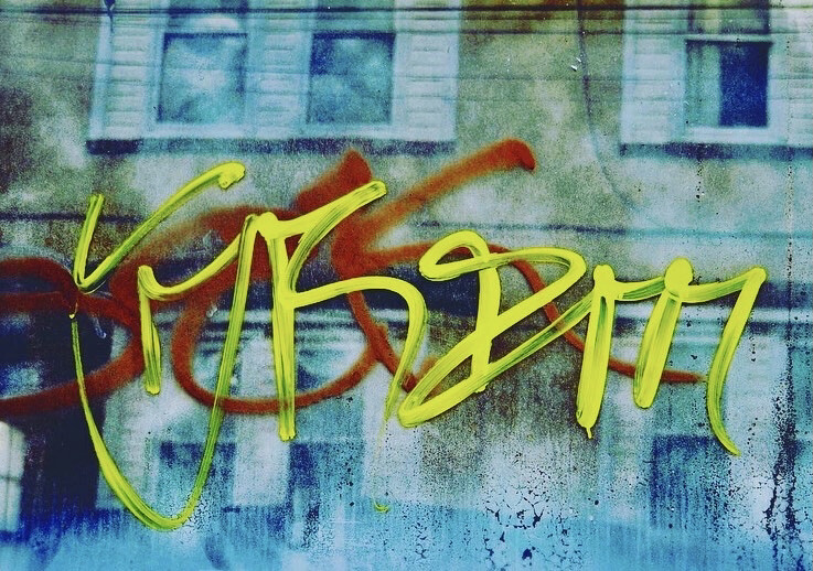 Graffiti atop a reflection of a building that shows several windows with shutters.