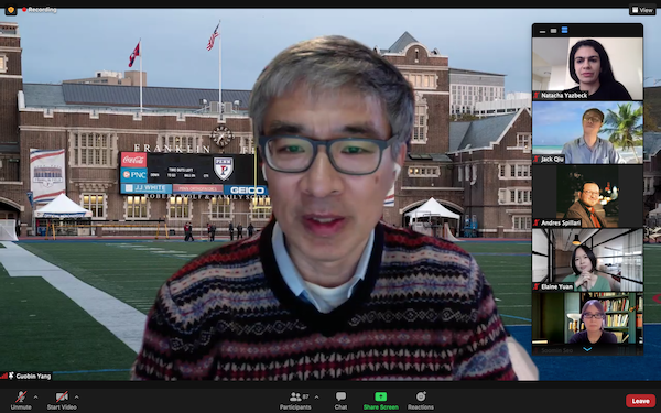 Person wearing glasses speaks on a Zoom call in front of a background featuring Penn's football stadium, as five others on the call are in a vertical column on the right side of the screen