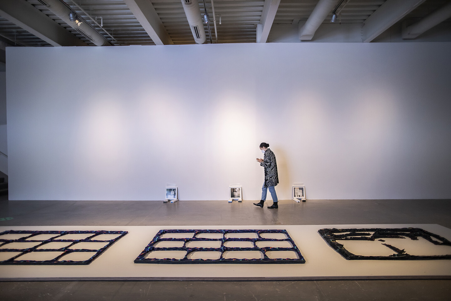 Artist walking through gallery with fabric works on floor and photos leaning against the wall
