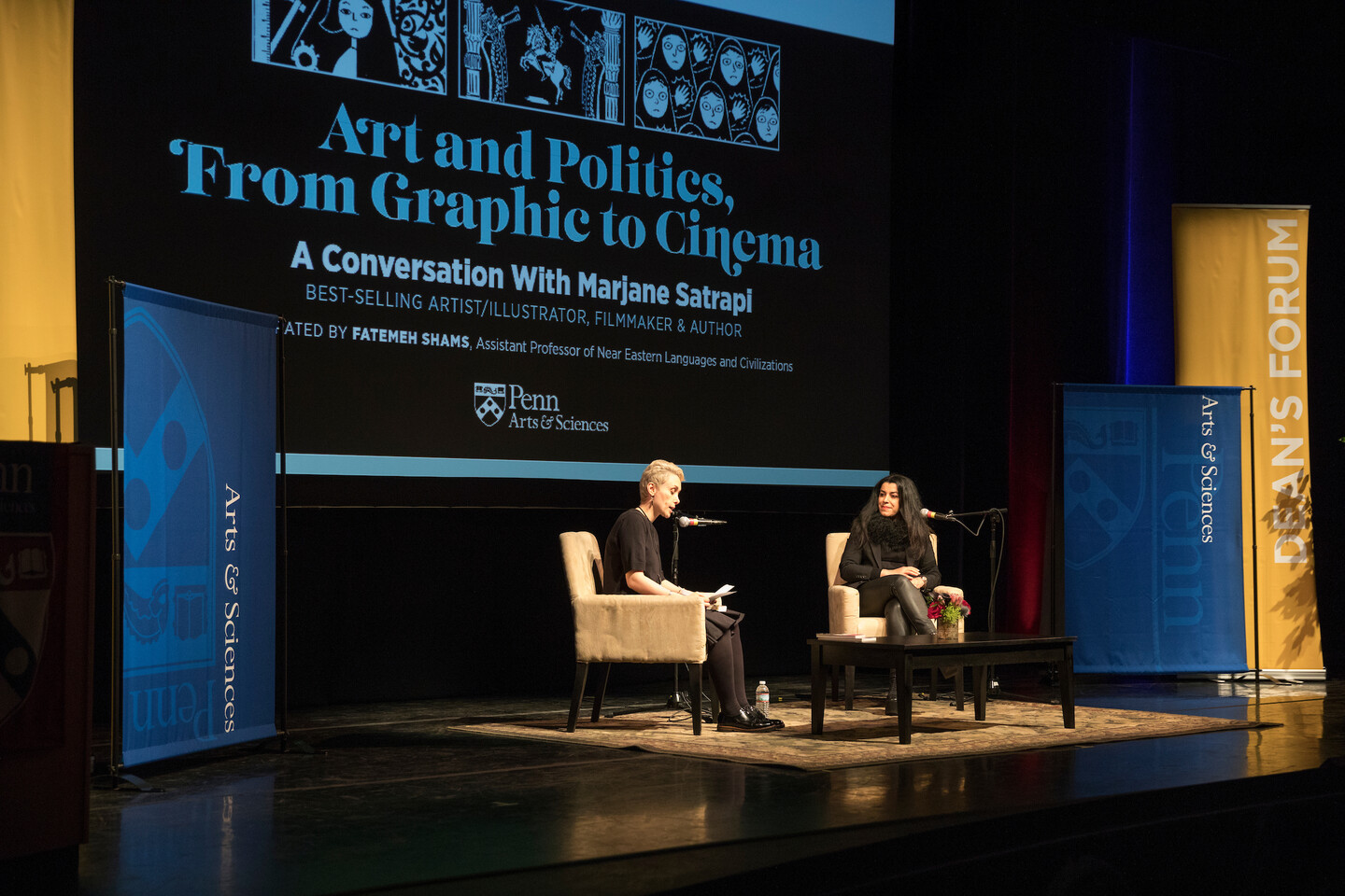 two people on a stage sitting in chairs talking
