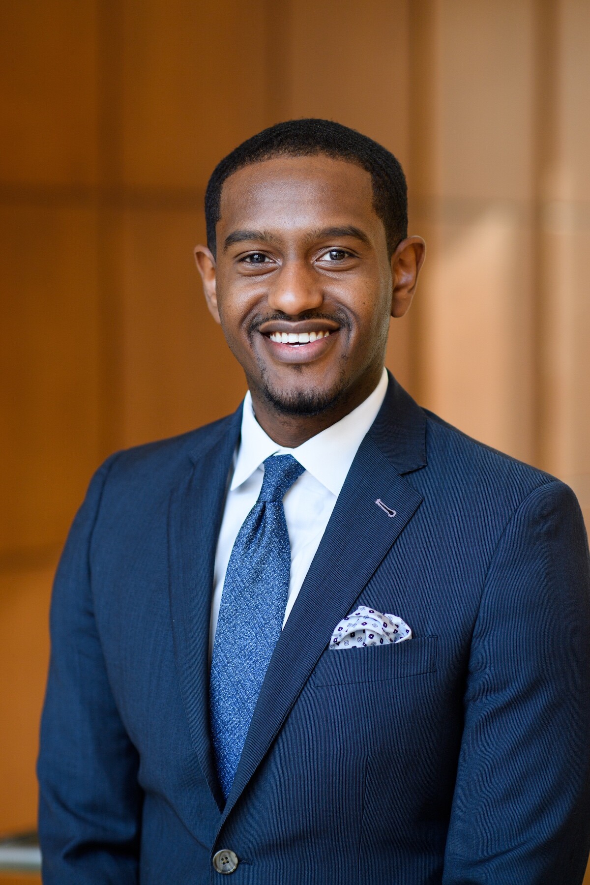 Man in blue suit with white shirt and blue tie smiles at the camera