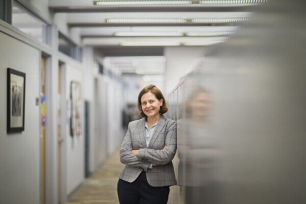 professor stands with arms folded in hallway