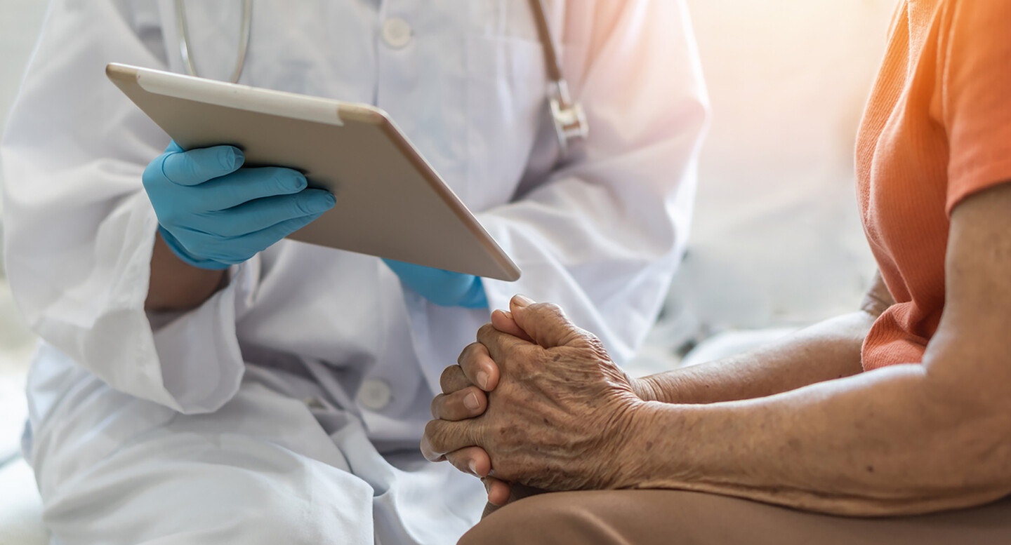 Person sitting with a doctor who is holding a computer tablet