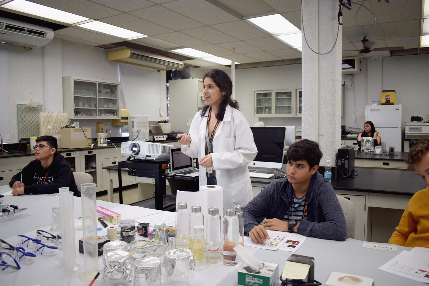 a person wearing a lab coat gives a lecture to students in a lab 