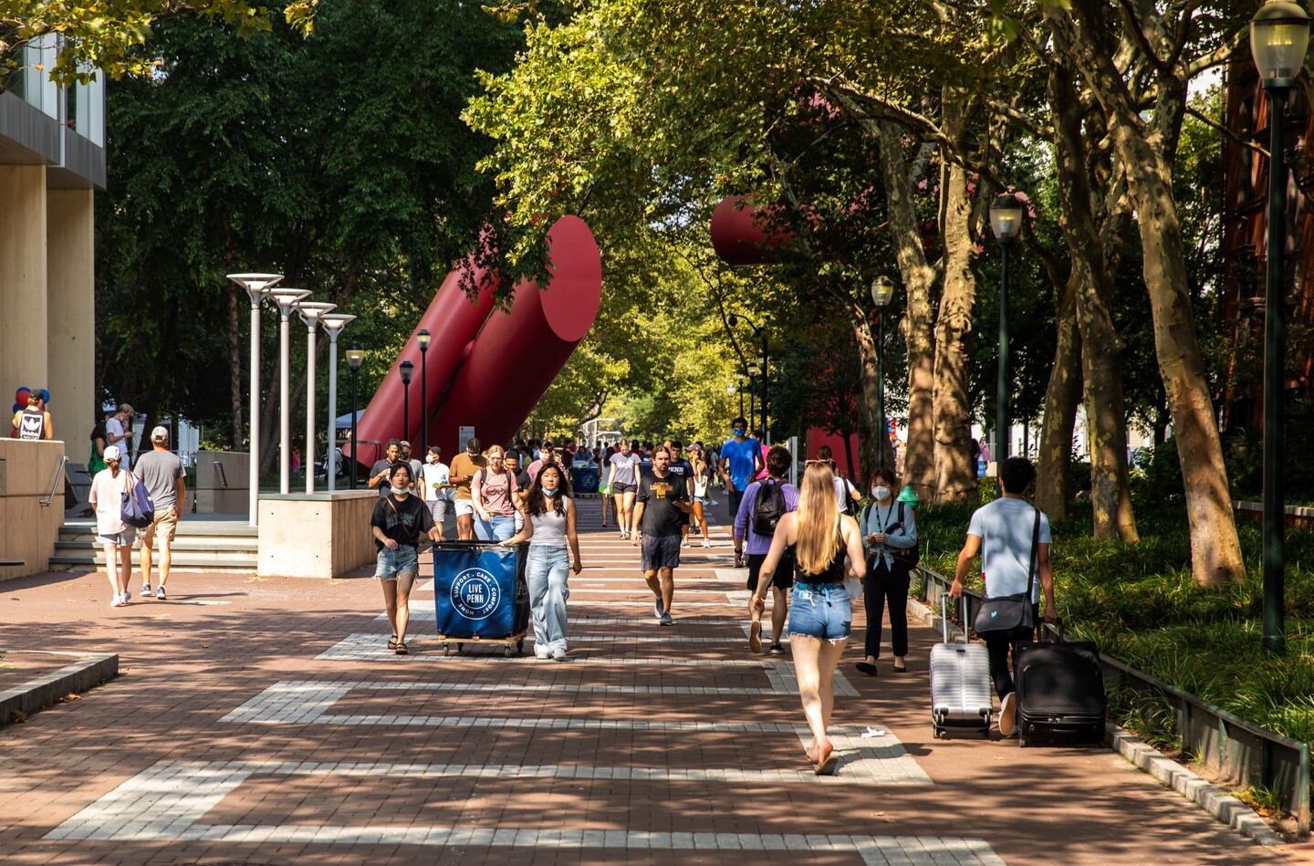 People strolling Locust Walk with suitcases and move-in carts