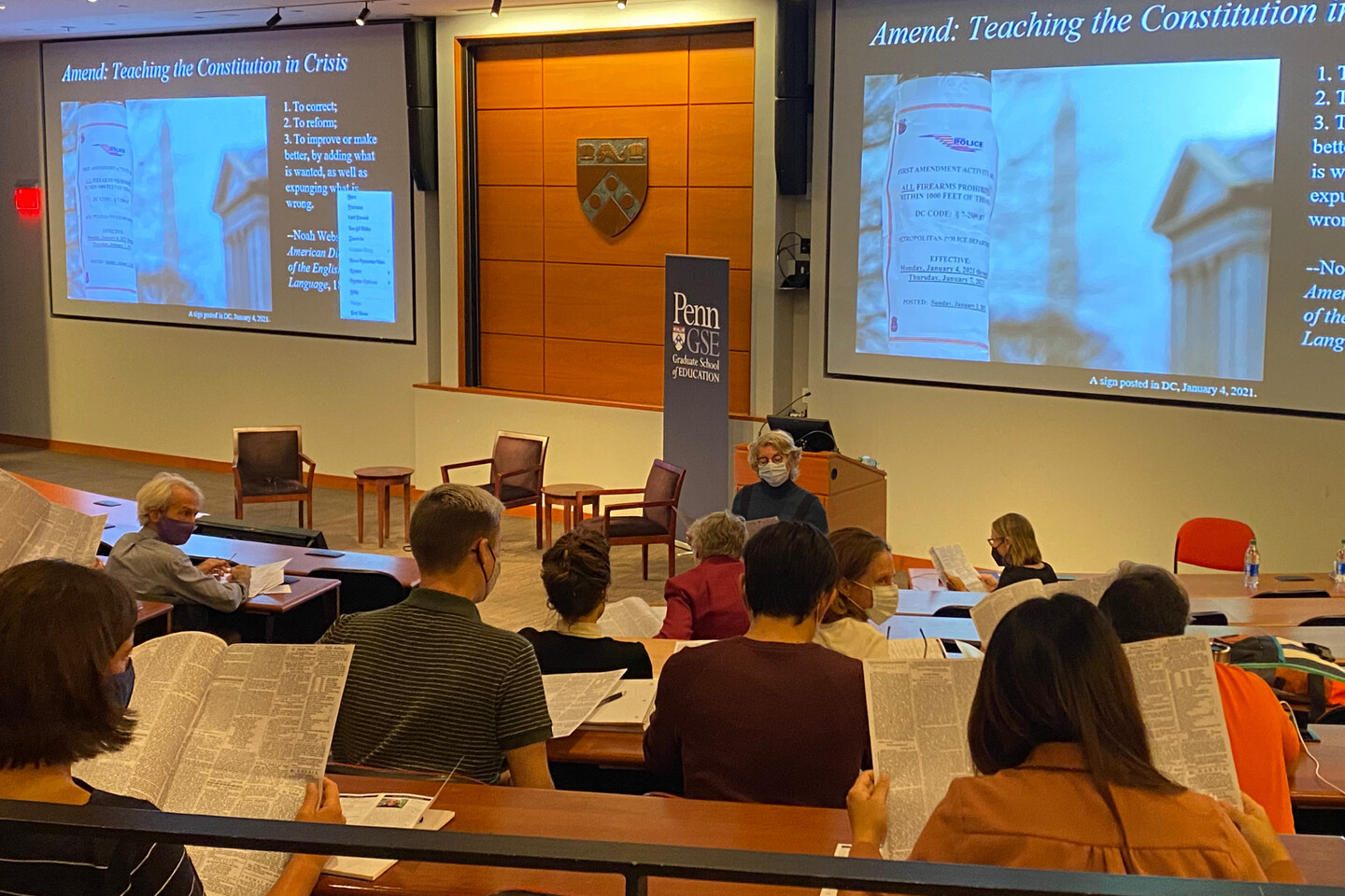 Professor in front of several people seated looking at copy of newspaper