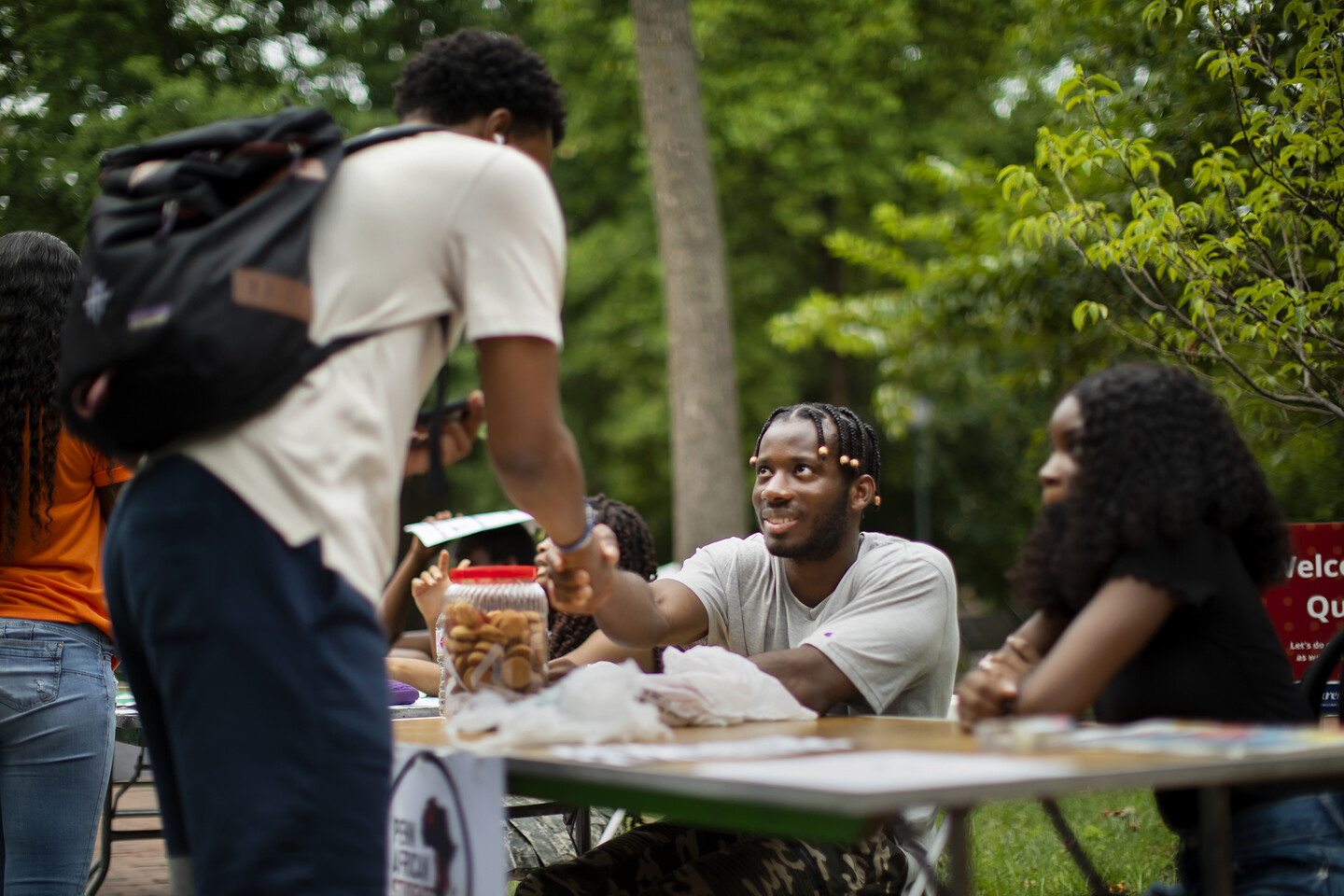 one student shaking the hand of another over a table outside 