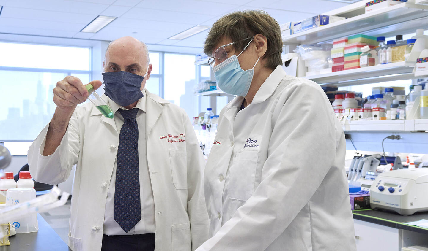 Drew Weisman and Katalin Kariko wear masks in a lab and look at liquid in a test tube.