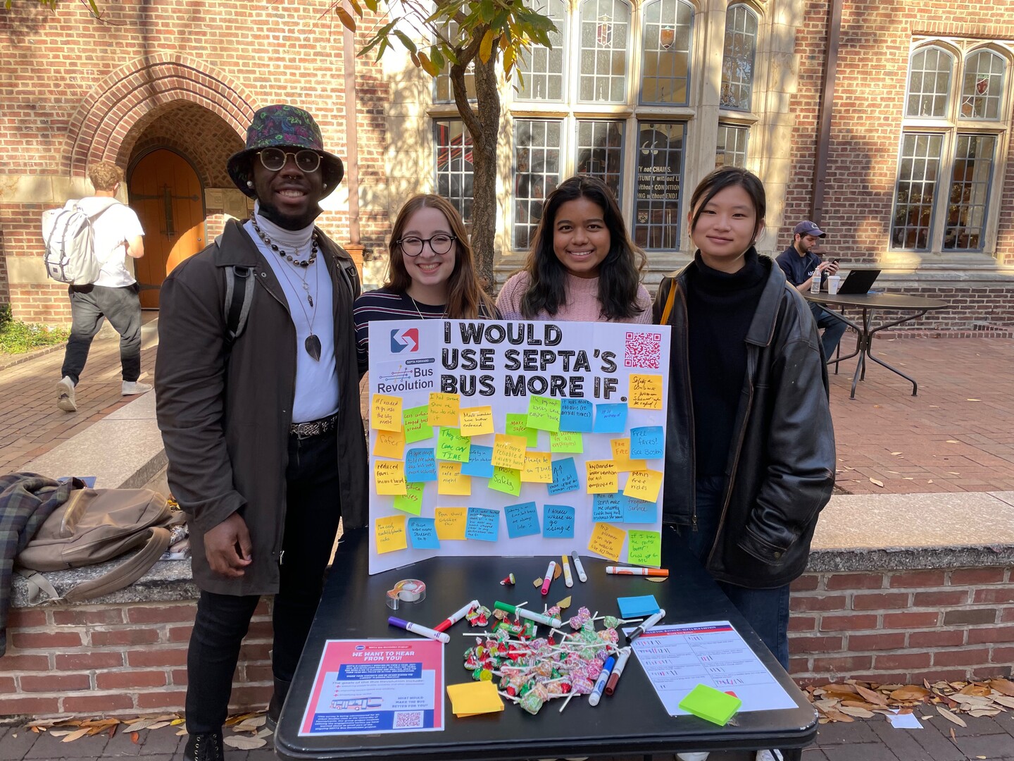 four people posing by a white board with sticky notes that says i would use SEPTA's bus more if...