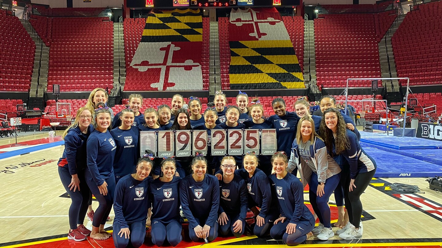 Members of the gymnastics team pose with a banner showing their score.