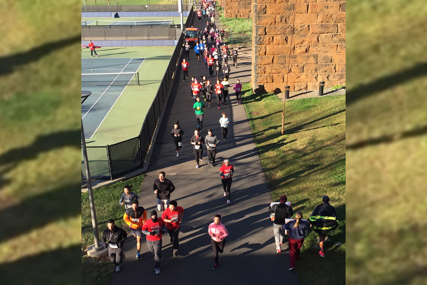 Aerial view of runners along a street with tennis courts on one side.