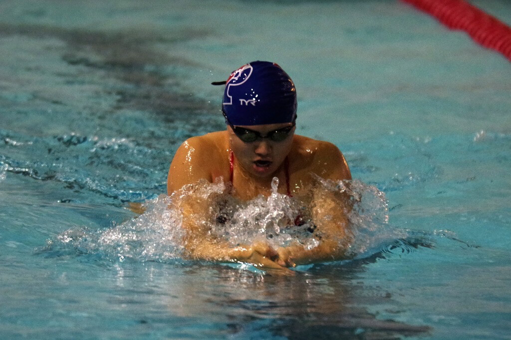 A woman rises up out of the pool to take a breath while performing the breast stroke