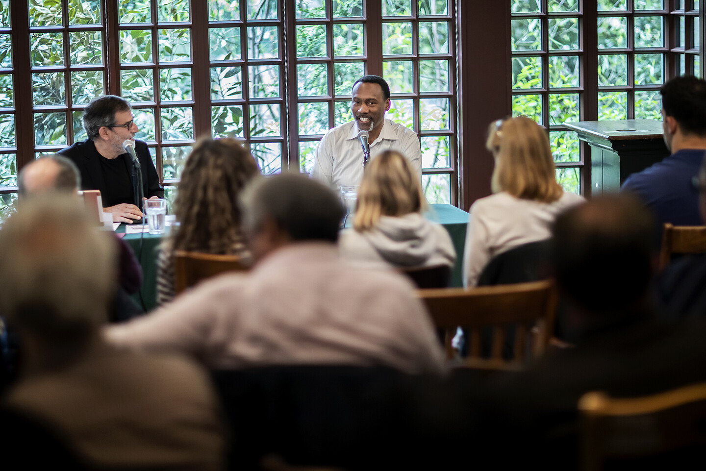 Al Filreis and Doug Glanville speaking in front of a wall of windows with the audience visible in front of them