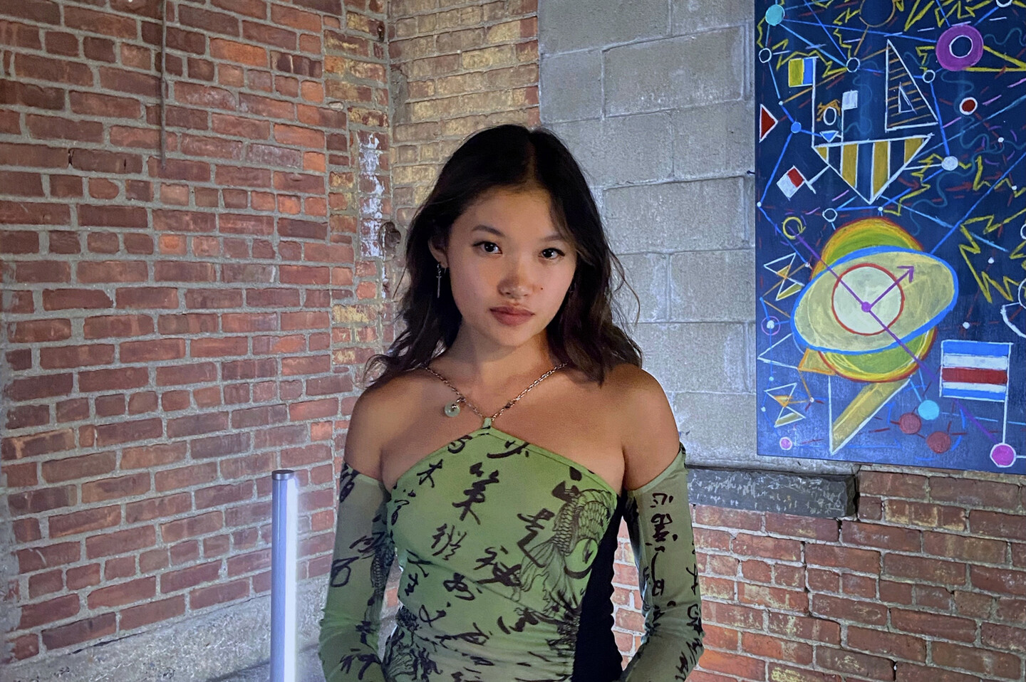 Annie Ma stands in front of a painting mounted on a brick wall.