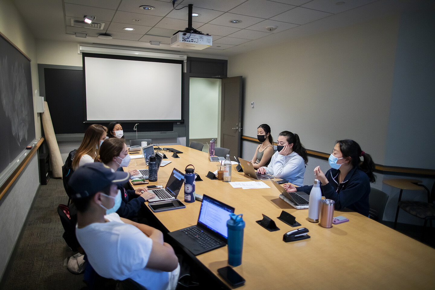 Students sit around a table looking at laptop computers