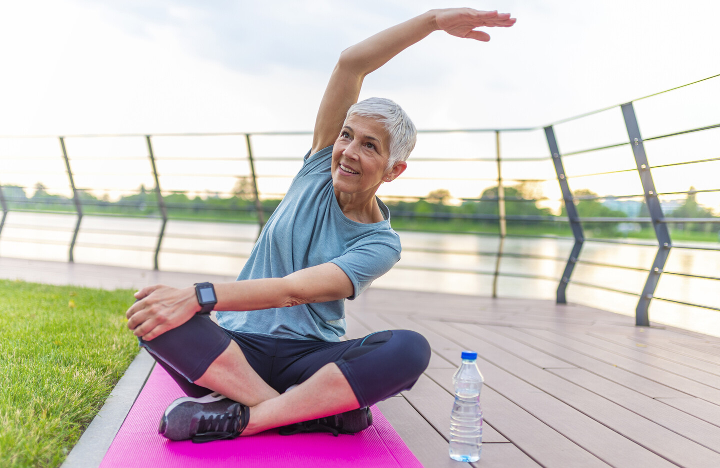 A person stretches on a yoga mat on an outdoor walkway.